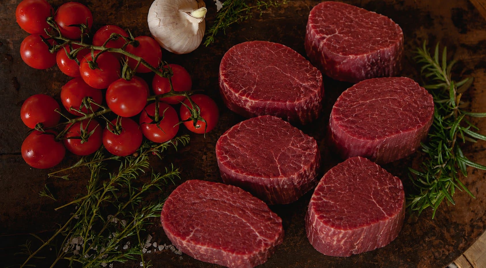 Sechs Aberdeen-Angus-Filet-Medaillons, roh, mit Strauchtomaten, Rosmarin und Knoblauch