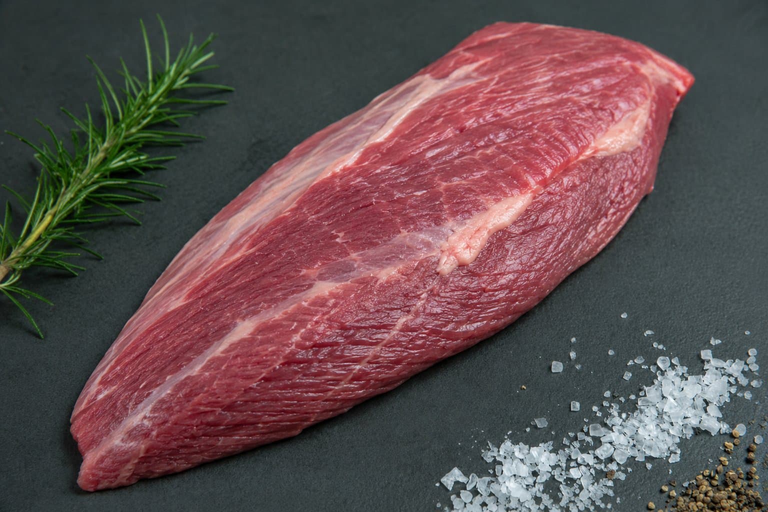 Tafelspitz vom Aberdeen Angus im Stück auf dunkler Fläche, mit feiner Fettkappe, Rosmarinzweig und Meersalz