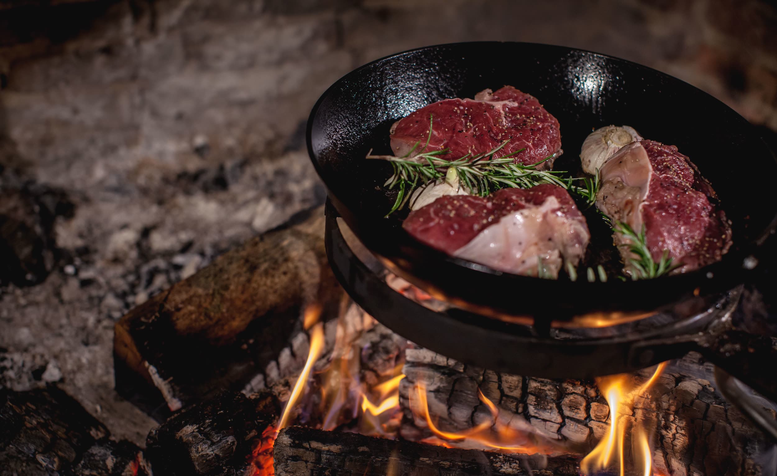 Steaks in der gusseisernen Pfanne über offenem Feuer