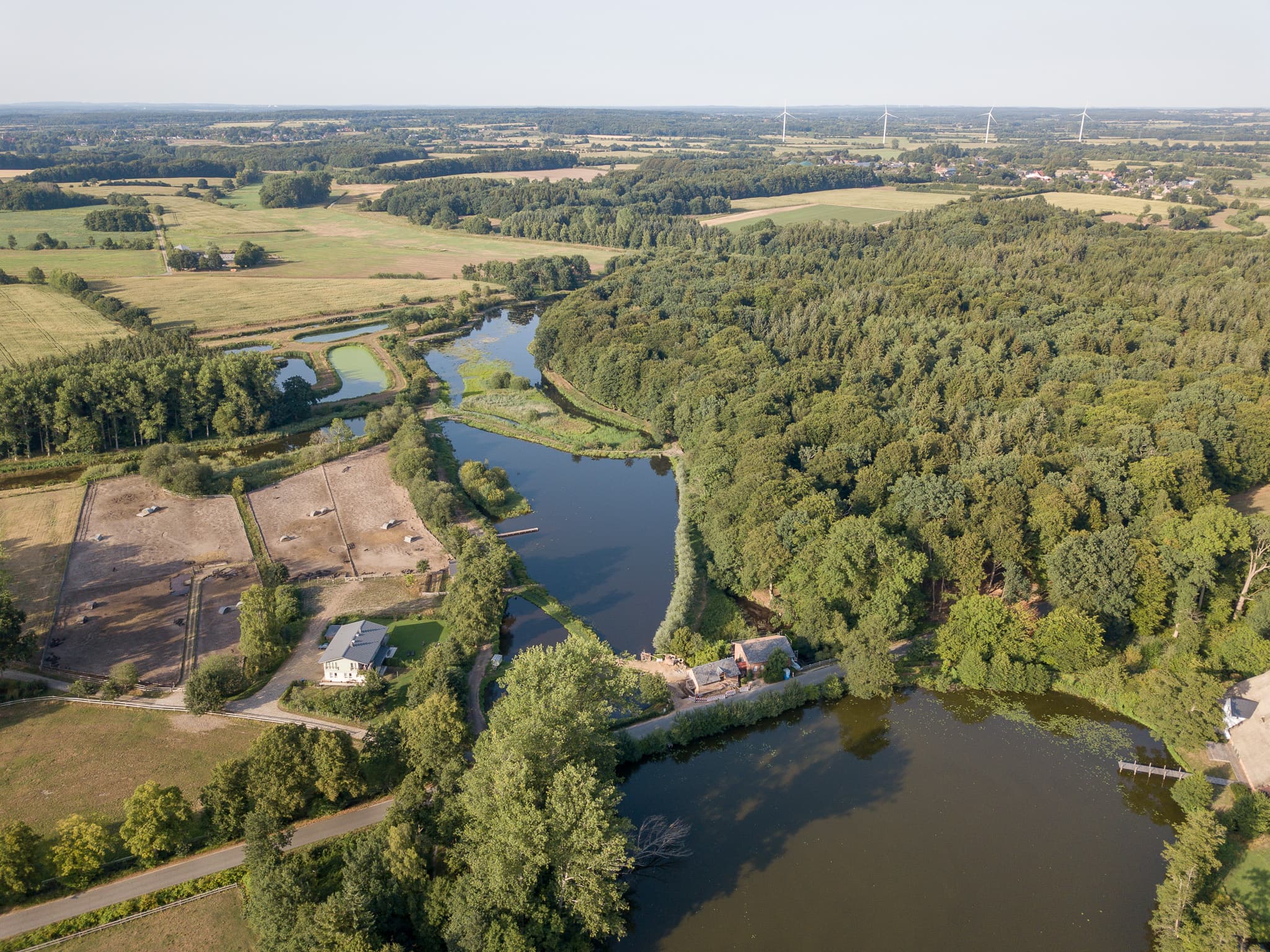 Weite Landschaft mit Wäldern und Wasserflächen rund um den Hof