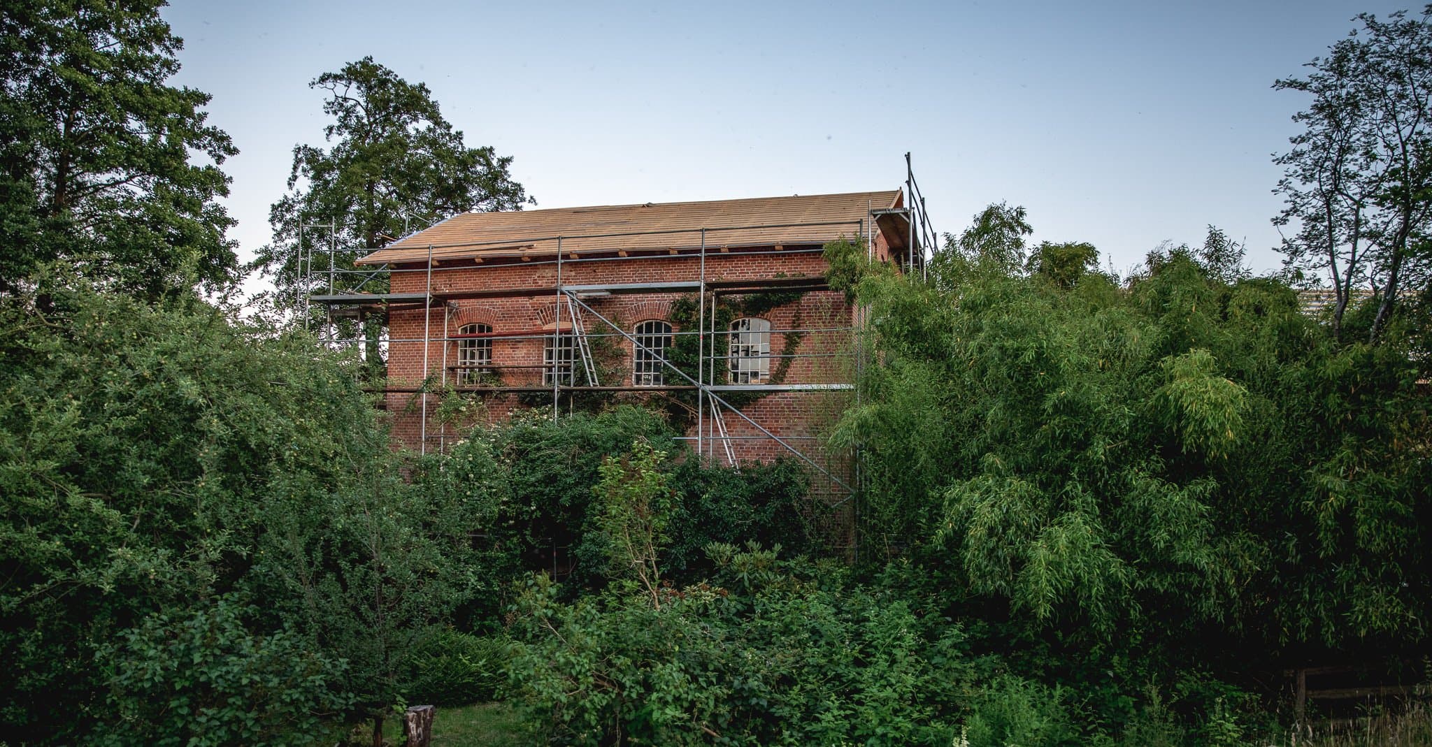 Backsteinhaus mit Gerüst, eingebettet in das Grün rund um den Hof